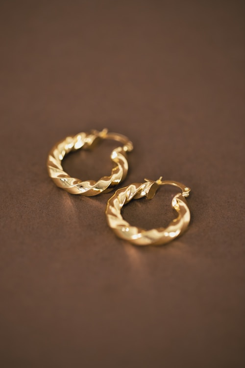 Pair of polished 24 K gold earrings stamped “999.9” resting on a dark surface.